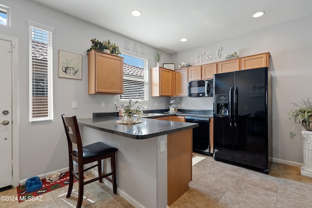 kitchen featuring kitchen peninsula, a breakfast bar area, light brown cabinetry, light tile patterned floors, and black appliances