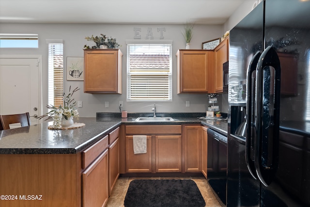 kitchen with kitchen peninsula, black refrigerator with ice dispenser, a healthy amount of sunlight, and sink