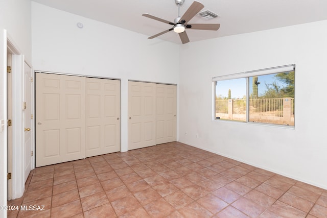 unfurnished bedroom featuring ceiling fan, light tile patterned floors, and two closets