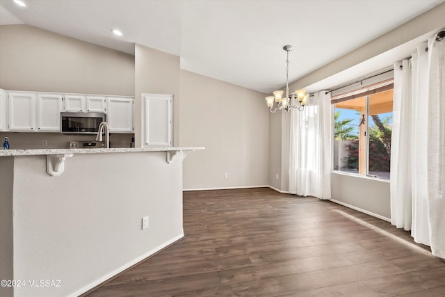 kitchen featuring pendant lighting, a breakfast bar, an inviting chandelier, vaulted ceiling, and white cabinetry