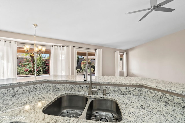 kitchen featuring pendant lighting, ceiling fan with notable chandelier, light stone counters, and sink