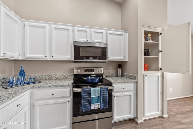 kitchen with white cabinetry, light wood-type flooring, light stone counters, and appliances with stainless steel finishes