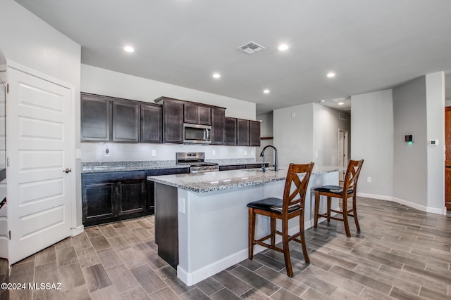 kitchen with a breakfast bar area, a kitchen island with sink, light hardwood / wood-style flooring, and stainless steel appliances