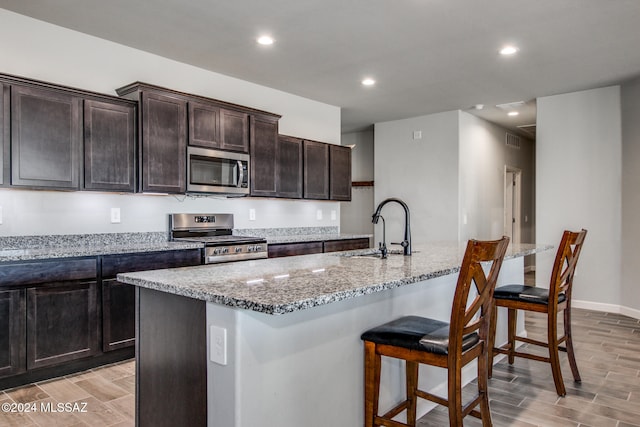 kitchen with a center island with sink, sink, appliances with stainless steel finishes, and light wood-type flooring