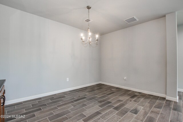 spare room featuring an inviting chandelier and dark wood-type flooring