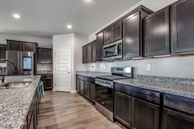 kitchen with light stone countertops, sink, appliances with stainless steel finishes, light wood-type flooring, and dark brown cabinetry