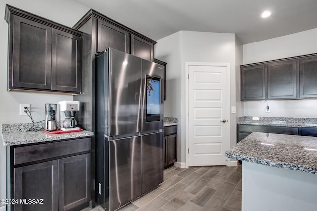 kitchen featuring stone countertops, wood-type flooring, dark brown cabinetry, and stainless steel fridge