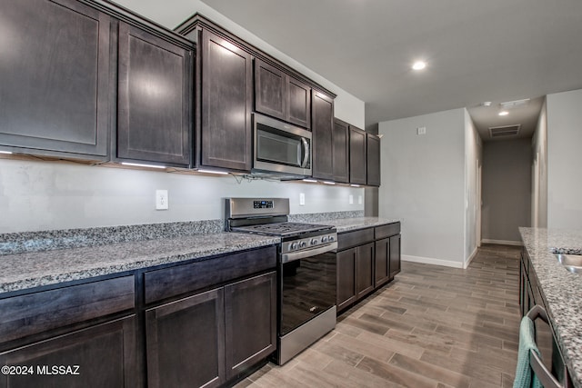 kitchen with dark brown cabinetry, stainless steel appliances, light stone countertops, and light wood-type flooring