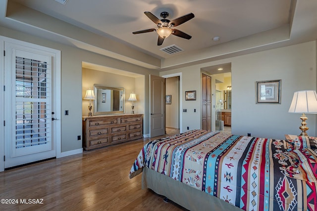 bedroom with access to exterior, a tray ceiling, ceiling fan, wood-type flooring, and connected bathroom