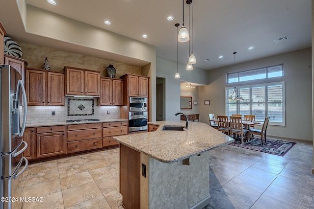 kitchen with pendant lighting, a center island with sink, sink, light stone countertops, and stainless steel appliances