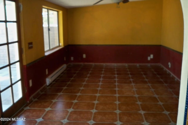 tiled spare room featuring a baseboard heating unit and ceiling fan