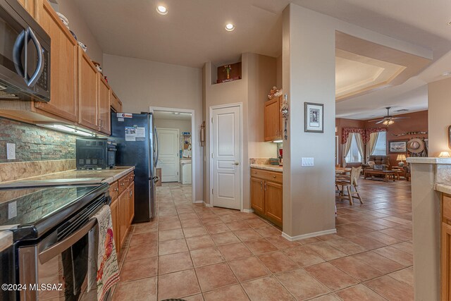 kitchen with ceiling fan, light tile patterned floors, decorative backsplash, stainless steel appliances, and a tray ceiling