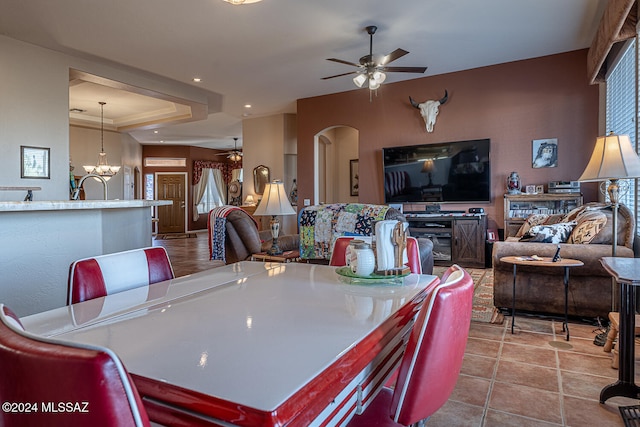 dining space with sink, ceiling fan with notable chandelier, and a raised ceiling