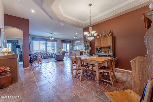 dining area with ceiling fan with notable chandelier, tile patterned floors, and a raised ceiling