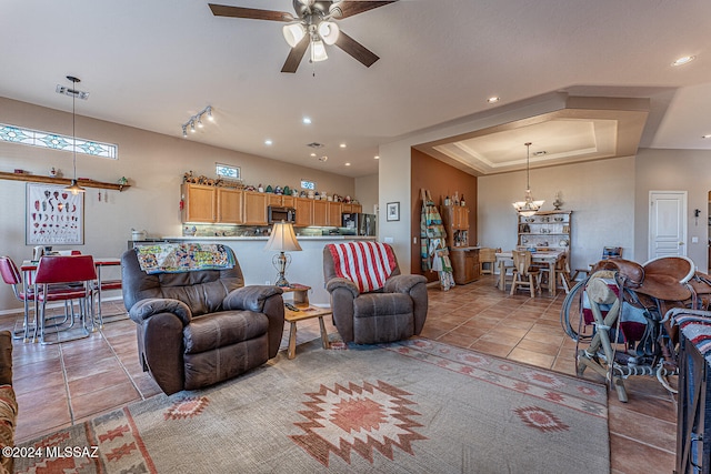 tiled living room featuring ceiling fan with notable chandelier, a raised ceiling, and rail lighting