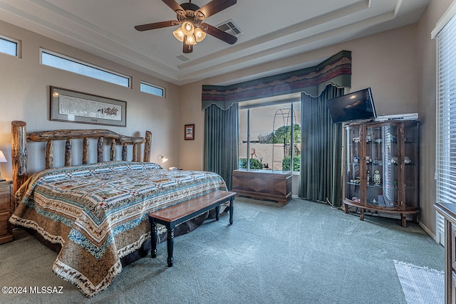 bedroom featuring ceiling fan, carpet, multiple windows, and a tray ceiling