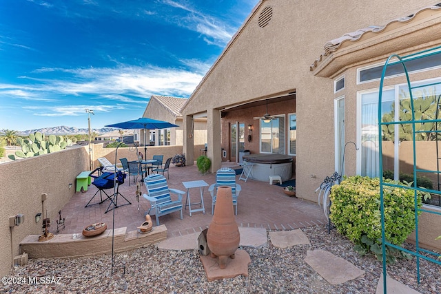 view of patio with a mountain view, a hot tub, and ceiling fan