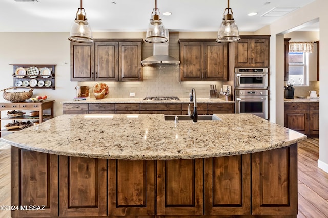 kitchen with wall chimney range hood, decorative backsplash, a kitchen island with sink, and sink