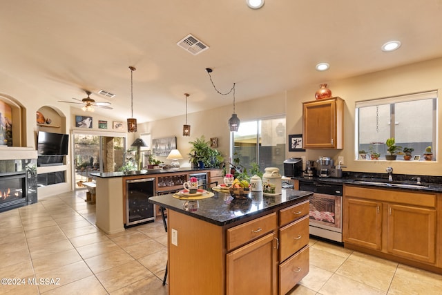 kitchen with a tile fireplace, ceiling fan, dishwasher, sink, and a center island with sink