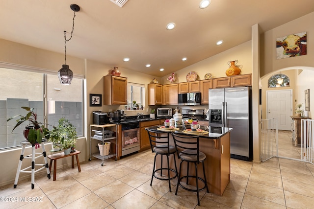 kitchen featuring light tile patterned flooring, lofted ceiling, hanging light fixtures, a kitchen island, and stainless steel appliances