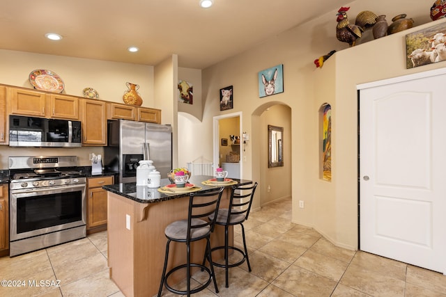 kitchen featuring light tile patterned floors, a breakfast bar area, dark stone countertops, stainless steel appliances, and a center island