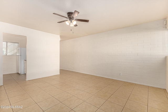 tiled empty room with ceiling fan and brick wall