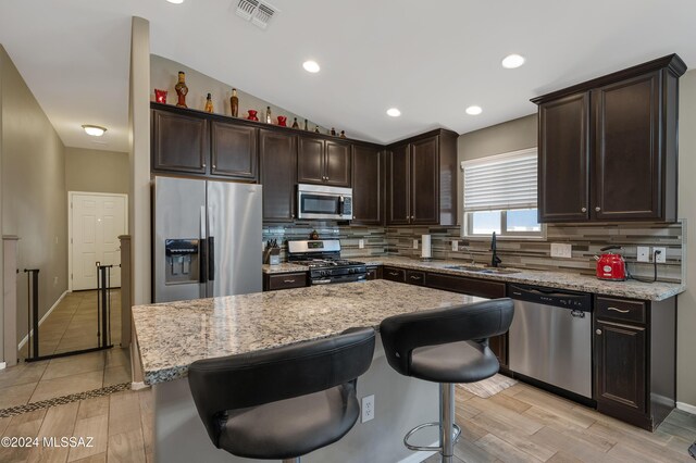 kitchen featuring stainless steel appliances, sink, a center island, light stone counters, and a breakfast bar