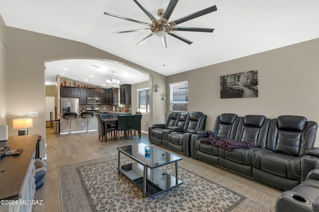 living room with lofted ceiling, ceiling fan with notable chandelier, and light wood-type flooring