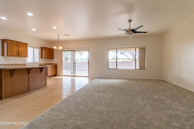 kitchen featuring ceiling fan with notable chandelier, light carpet, decorative light fixtures, and a breakfast bar area