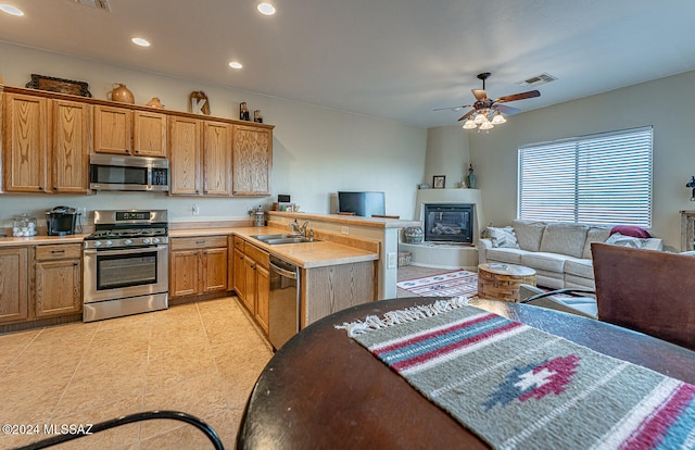 kitchen featuring sink, a large fireplace, kitchen peninsula, ceiling fan, and stainless steel appliances