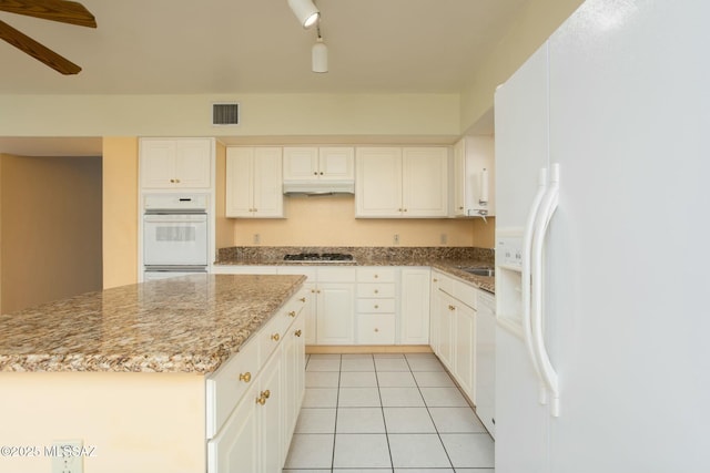 kitchen featuring track lighting, light stone counters, white appliances, a center island, and white cabinetry