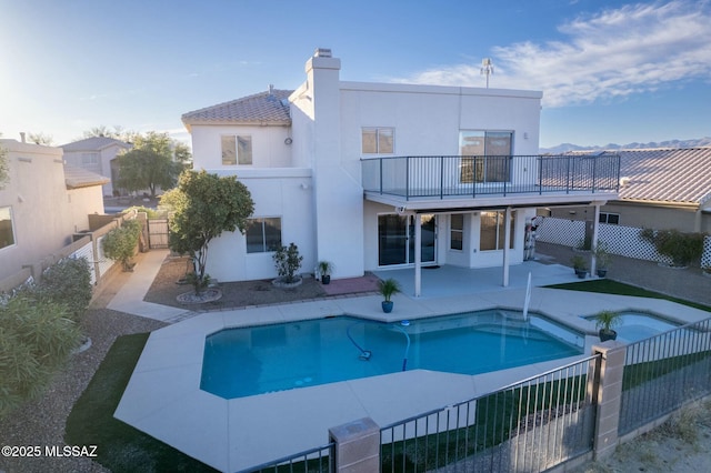 rear view of property with a swimming pool with hot tub, a patio, and a balcony