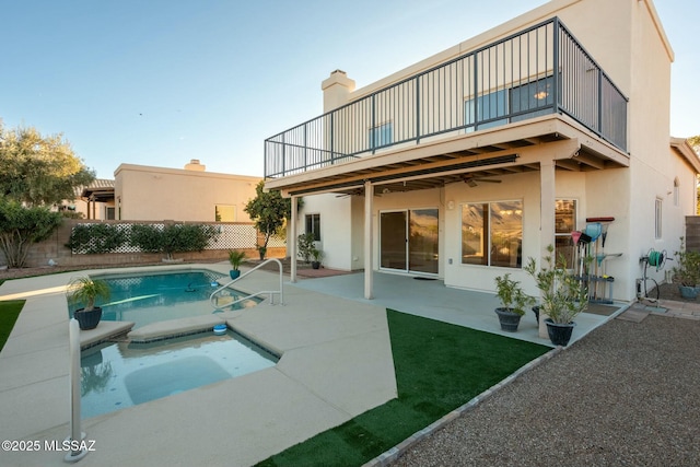 rear view of house with ceiling fan, a balcony, a patio, and a pool with hot tub