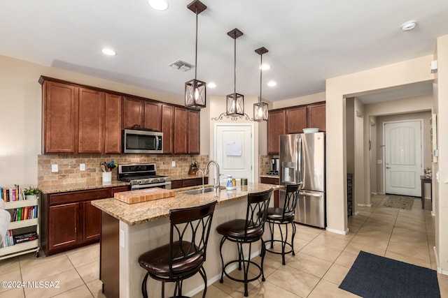 kitchen featuring light stone counters, a kitchen island with sink, sink, pendant lighting, and stainless steel appliances