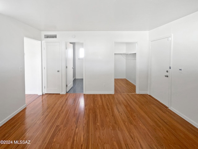 unfurnished bedroom featuring a closet, a walk in closet, and hardwood / wood-style flooring