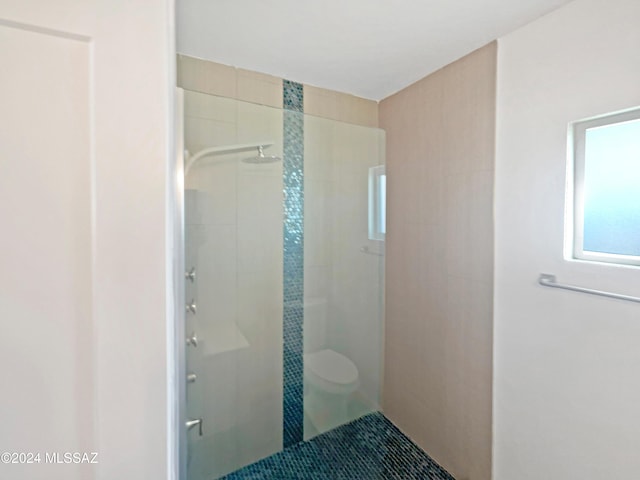 bathroom featuring toilet, a wealth of natural light, tiled shower, and tile patterned flooring