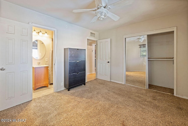 unfurnished bedroom featuring a closet, sink, light colored carpet, ensuite bathroom, and ceiling fan