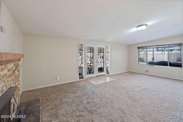 unfurnished living room with french doors, vaulted ceiling, a brick fireplace, and carpet floors