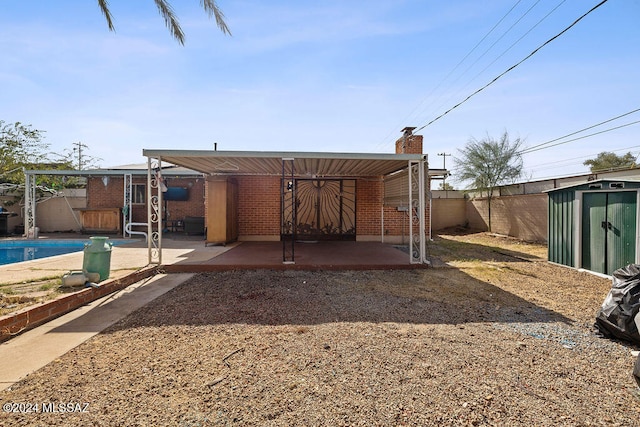 rear view of house featuring a patio area, a storage unit, and a fenced in pool