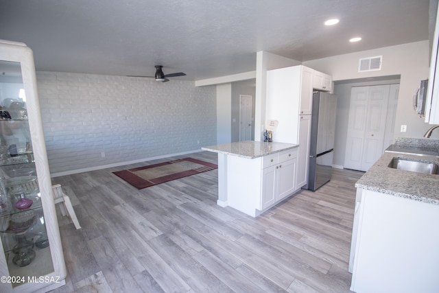 kitchen with stainless steel refrigerator, white cabinetry, sink, and brick wall