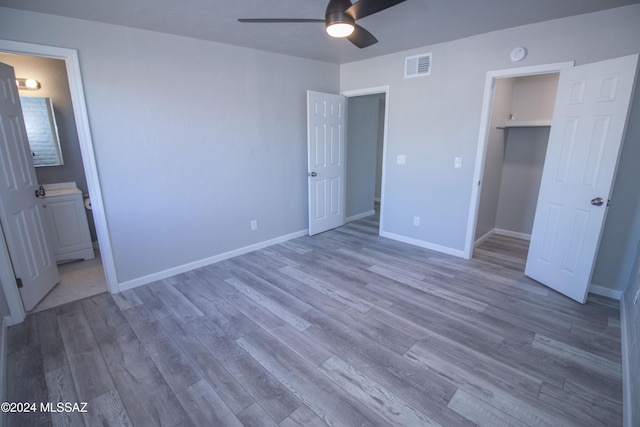 unfurnished bedroom featuring ensuite bath, ceiling fan, a spacious closet, wood-type flooring, and a closet