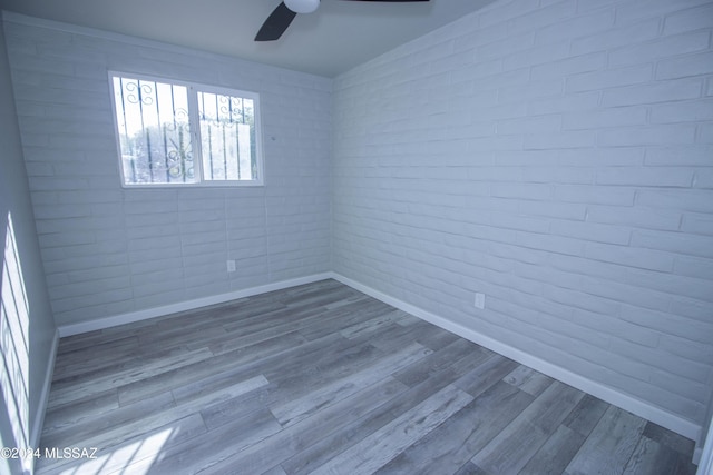 empty room with hardwood / wood-style flooring, ceiling fan, and brick wall