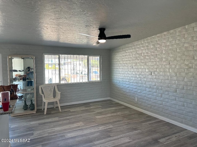 spare room with hardwood / wood-style floors, a textured ceiling, ceiling fan, and brick wall