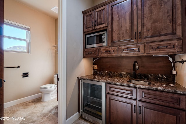 interior space featuring stainless steel microwave, a sink, dark brown cabinets, dark stone counters, and beverage cooler