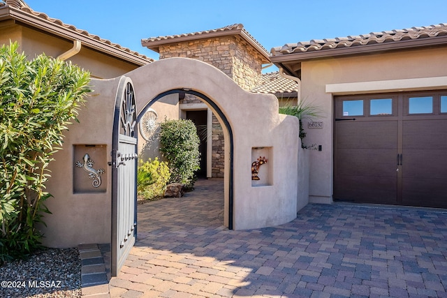 property entrance featuring a garage, stone siding, a tile roof, and stucco siding