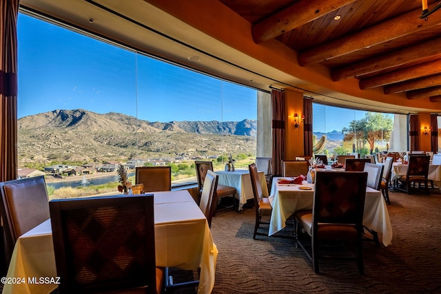 dining area featuring a mountain view, dark colored carpet, and beam ceiling