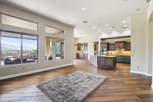 kitchen with dark wood-style flooring, tasteful backsplash, open floor plan, a kitchen island with sink, and dark brown cabinetry