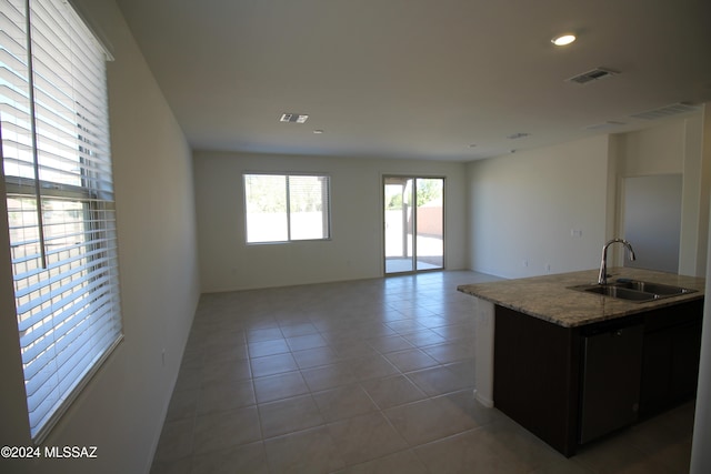 interior space featuring tile patterned floors, light stone counters, a center island with sink, black dishwasher, and sink