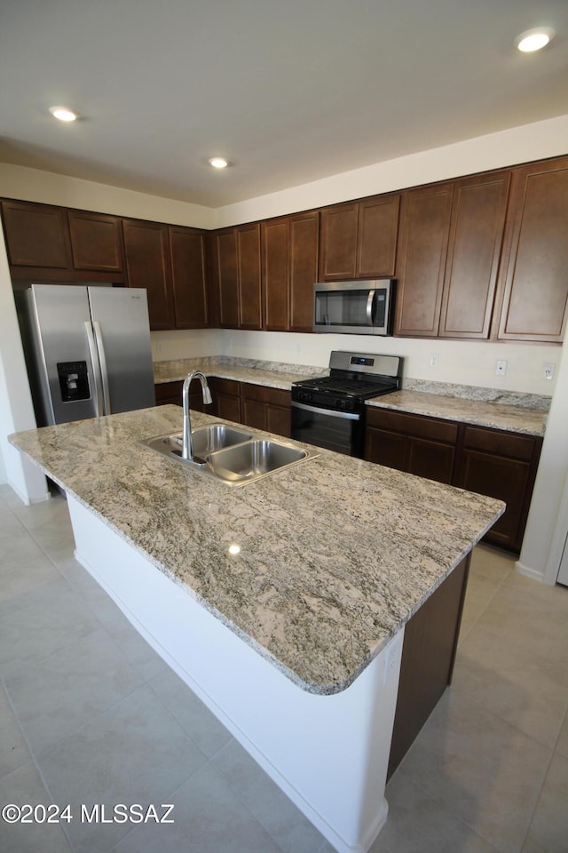 kitchen with a kitchen bar, stainless steel appliances, light stone counters, sink, and an island with sink