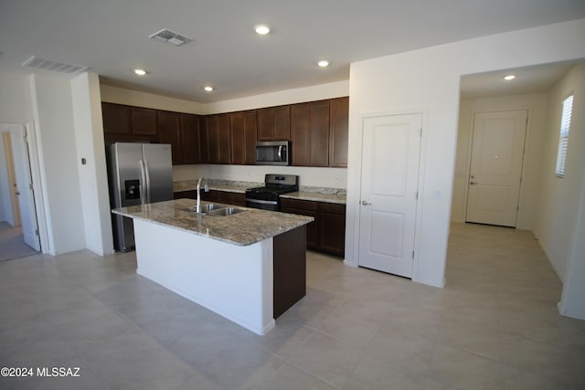 kitchen featuring sink, light stone counters, appliances with stainless steel finishes, dark brown cabinets, and a kitchen island with sink